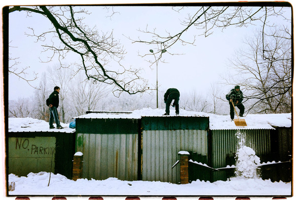 Grown men shoveling snow off garage roofs