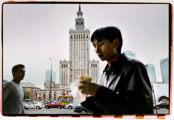 Asian guy eating shawarma in front of the Warsaw Palace of Culture.