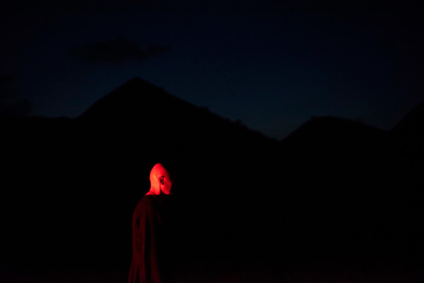 A man stands far away and in the dark, his head illuminated by a red light