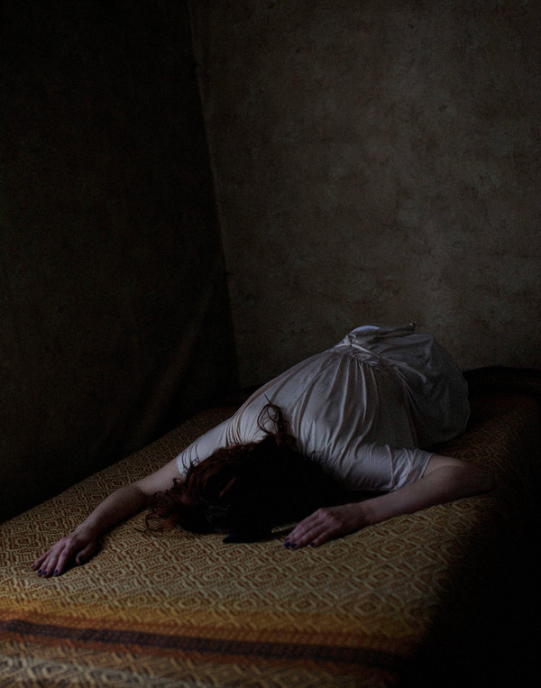 The girl lies head down on the bed, the colors dark and dull